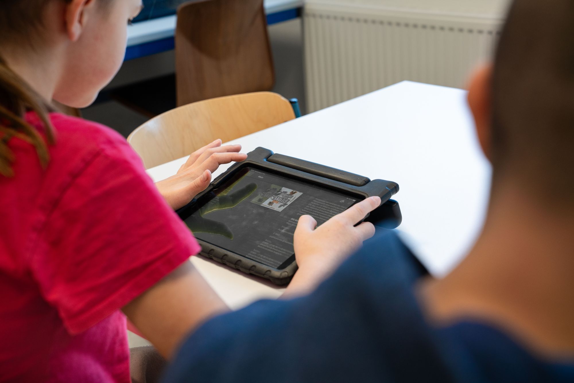 2 Kinder sitzen am Tisch und nutzen Tablets im Unterricht und schauen auf den Bildschirm