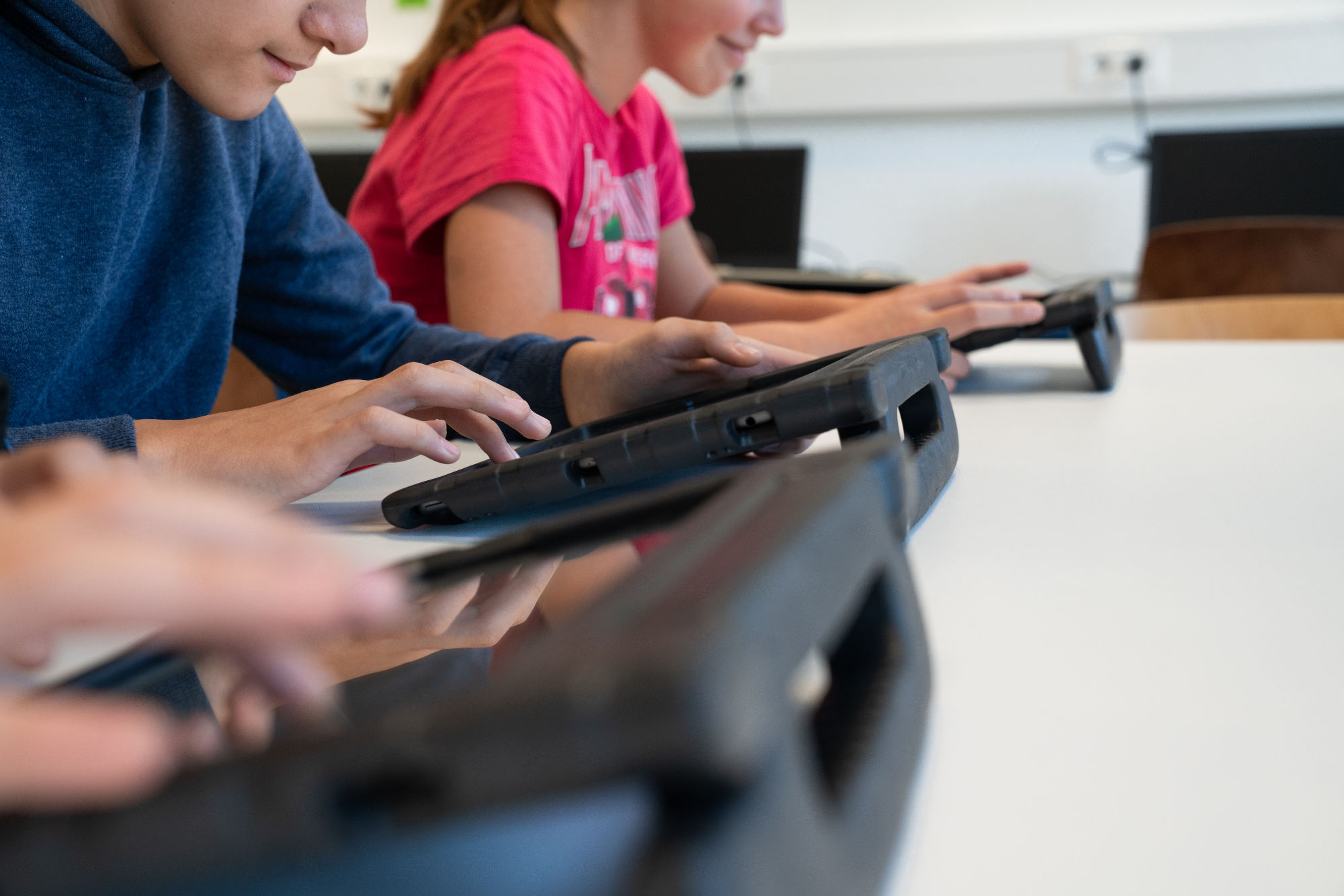 3 Schüler tippen auf ihren Tablett-Computern von der Seite beobachtet