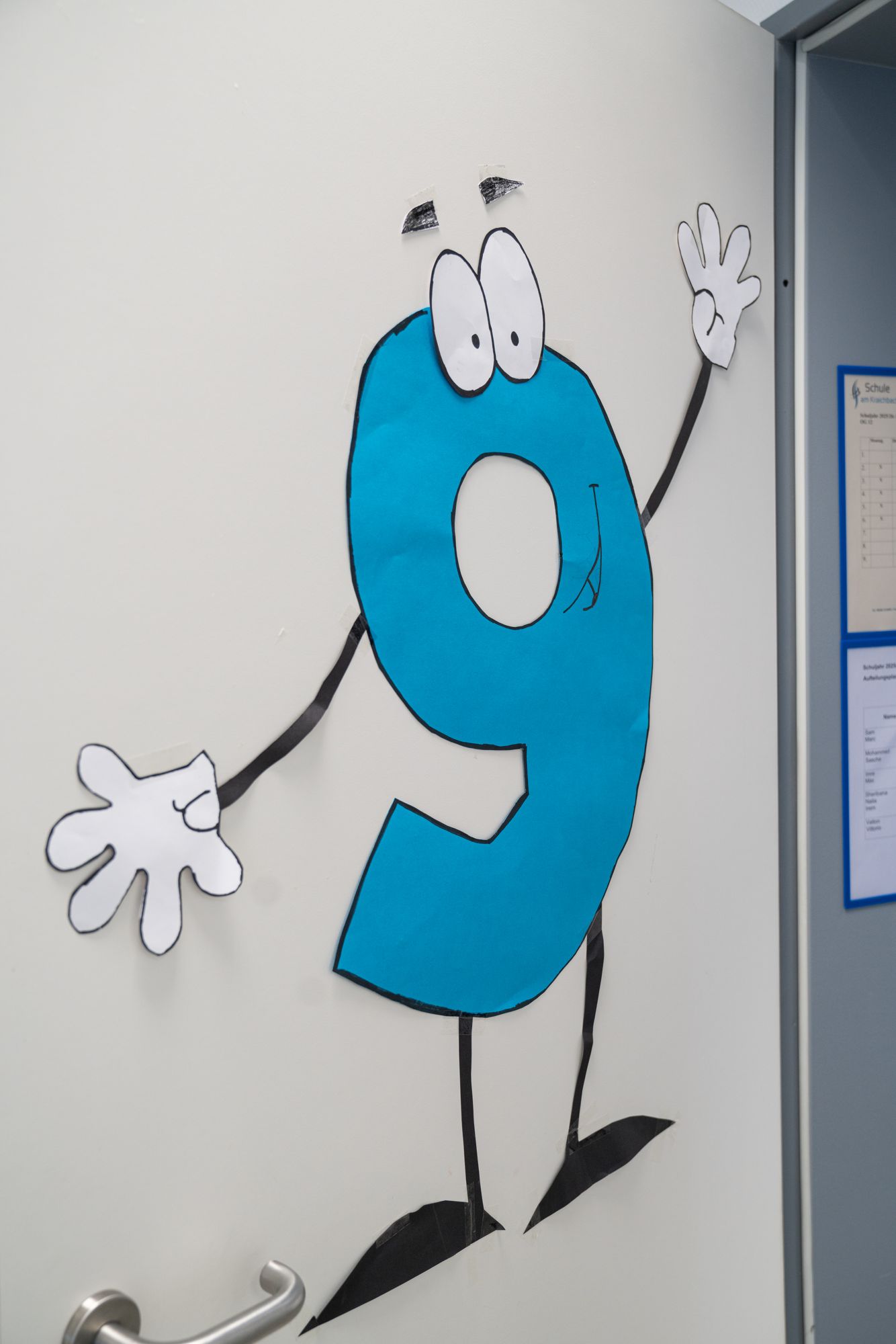 Auf einer weißen Tür klebt eine große blaue Zahl 9 mit Augen und Armen