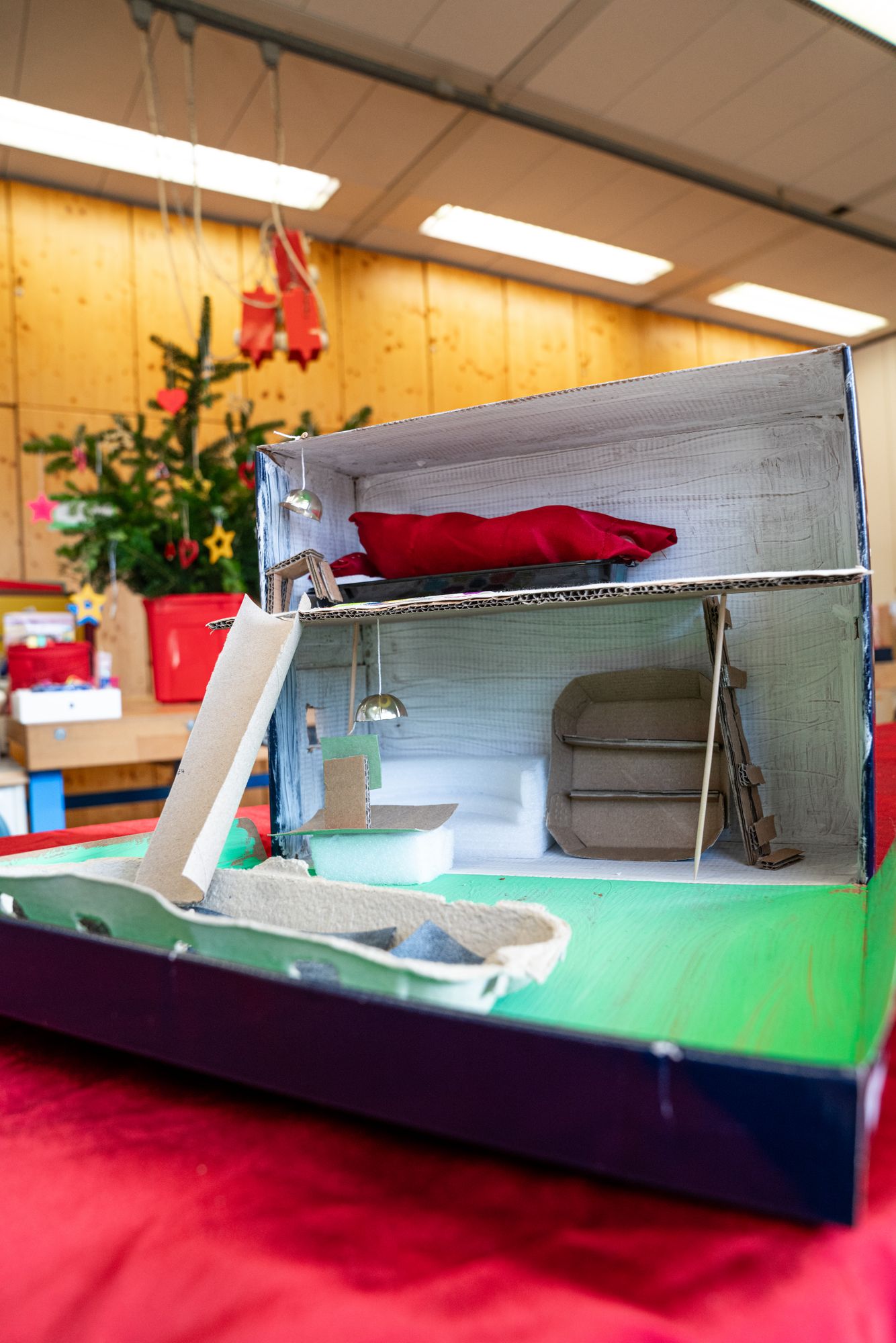 Ein Karton Zimmer Modell liegt auf rotem Tuch und im Hintergrund steht ein Weihnachtsbaum