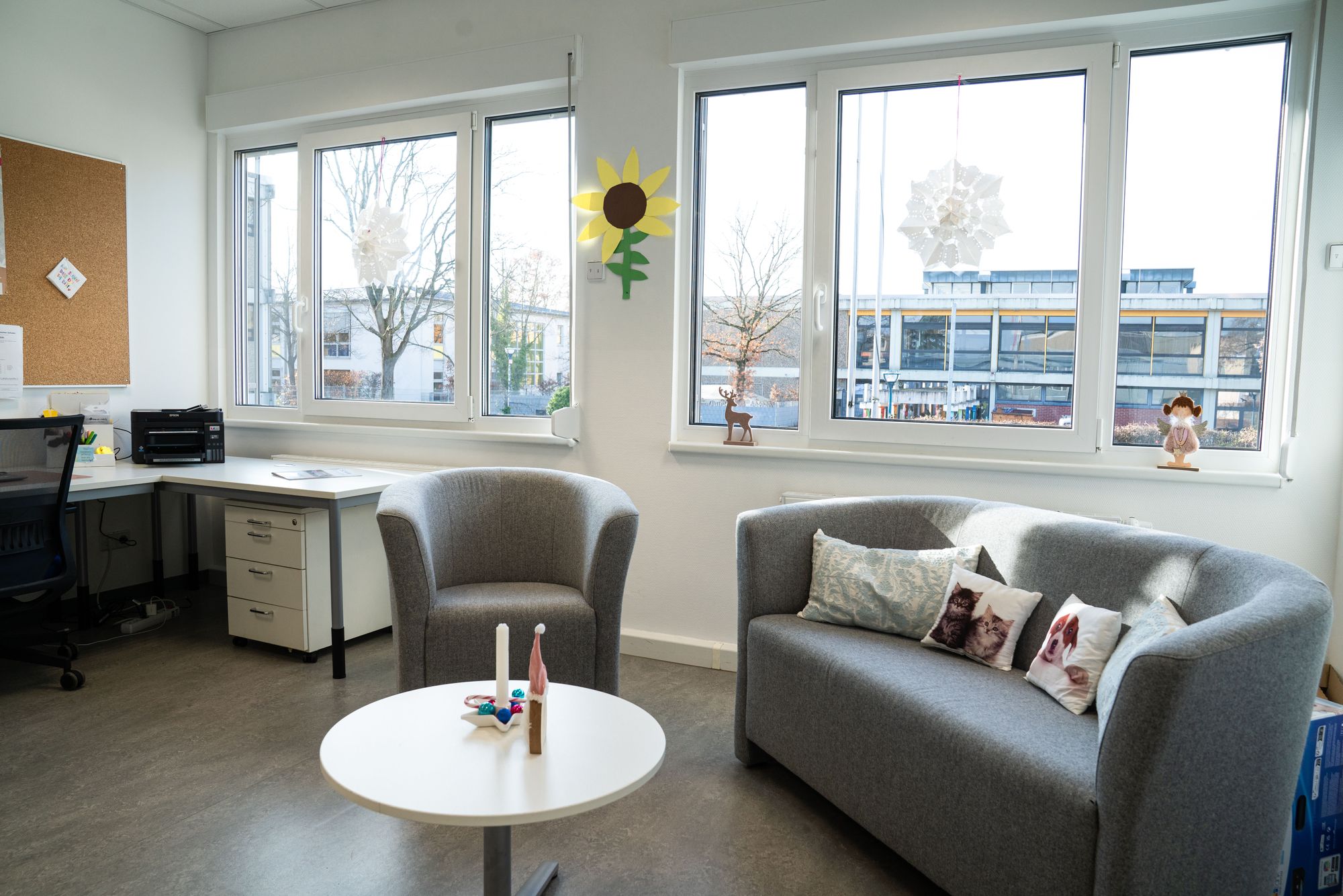 Ein heller Raum hat ein graues Sofa und einen Sessel und vorne steht ein runder Tisch