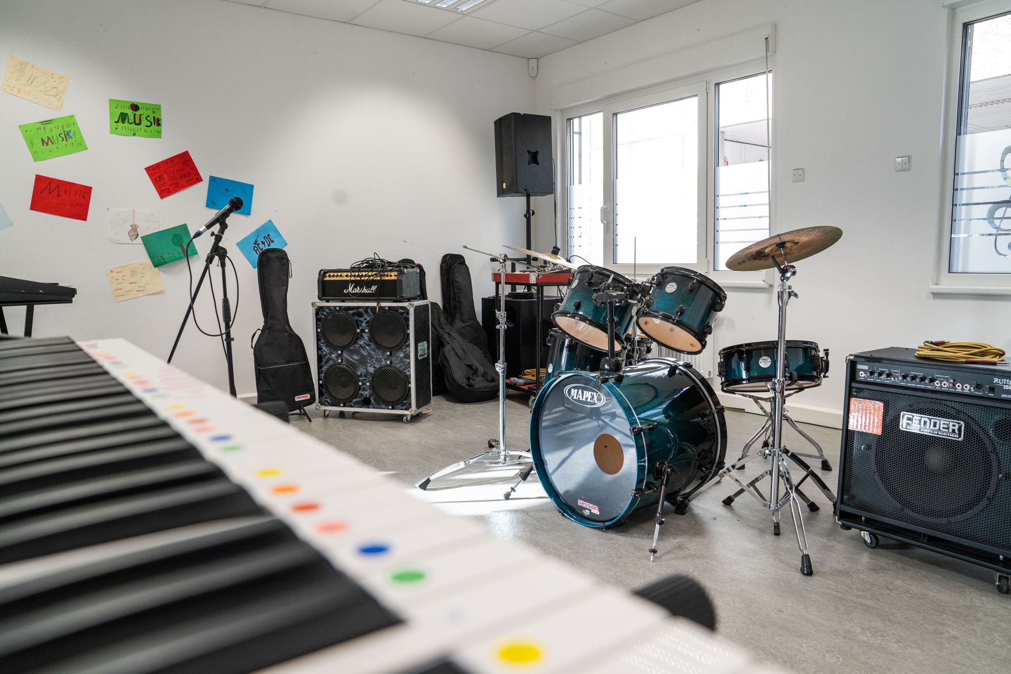 Im Musikraum stehen Schlagzeug Verstärker und Mikrofone und an der Wand hängen bunte Zettel