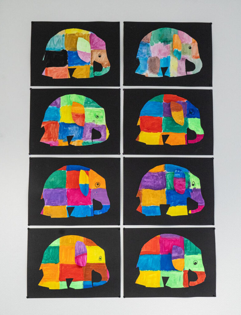 An der Wand hängen 6 bunte Elefanten Bilder auf schwarzem Papier und darunter 2 Zeichnungen
