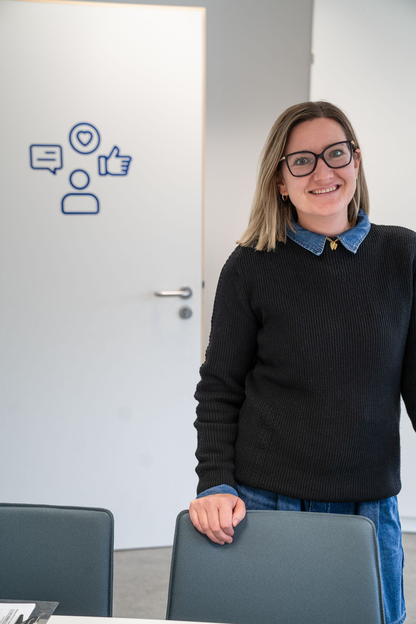 Schulsozialarbeiterin Frau Schlitt mit Brille lächelt freundlich und steht vor einer Tür mit blauen Symbolen